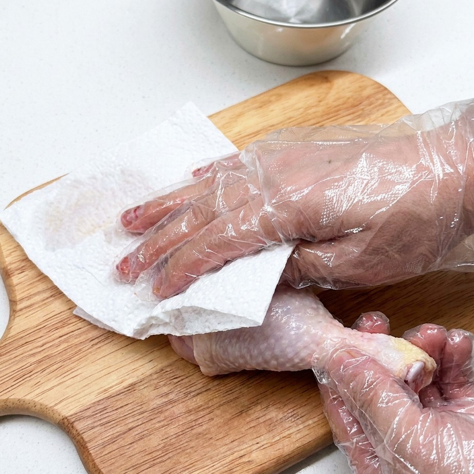 Muslo de pollo crudo siendo preparado sobre una tabla de cortar de madera con toallas de papel.