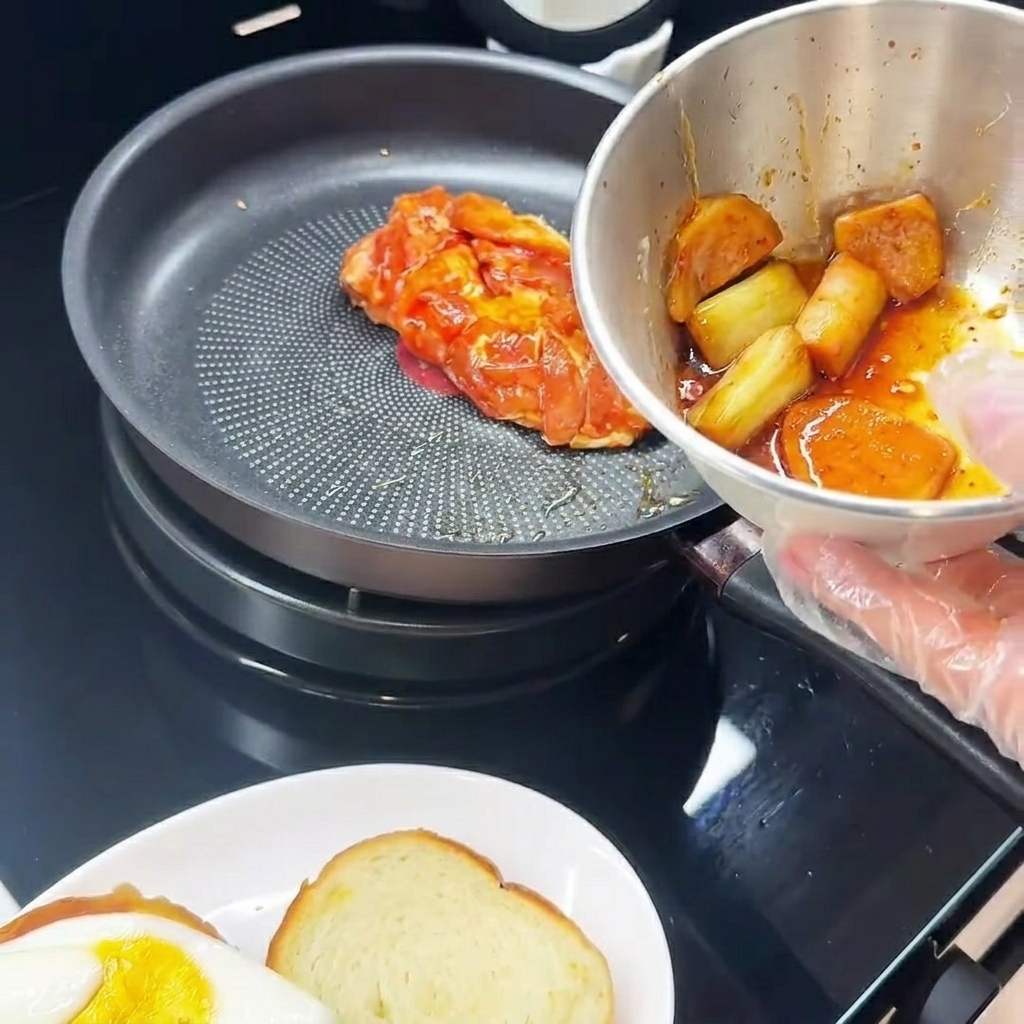 Muslo de pollo marinado cocinándose en una sartén, con el lado de la piel hacia abajo, junto a un plato con un huevo frito.