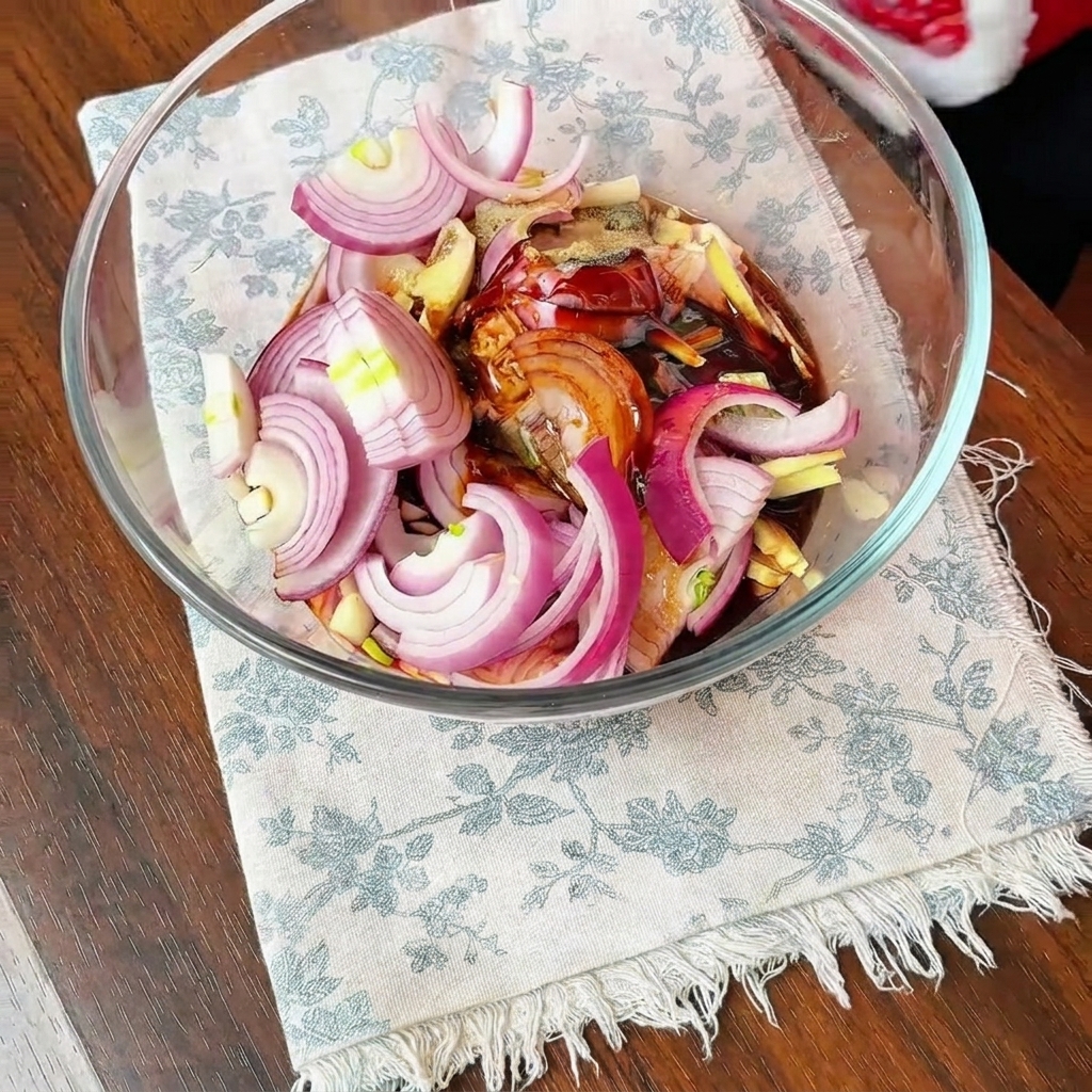 Contramuslos de pollo, cebollas en rodajas y condimentos de la marinada mezclados en un tazón grande de vidrio.