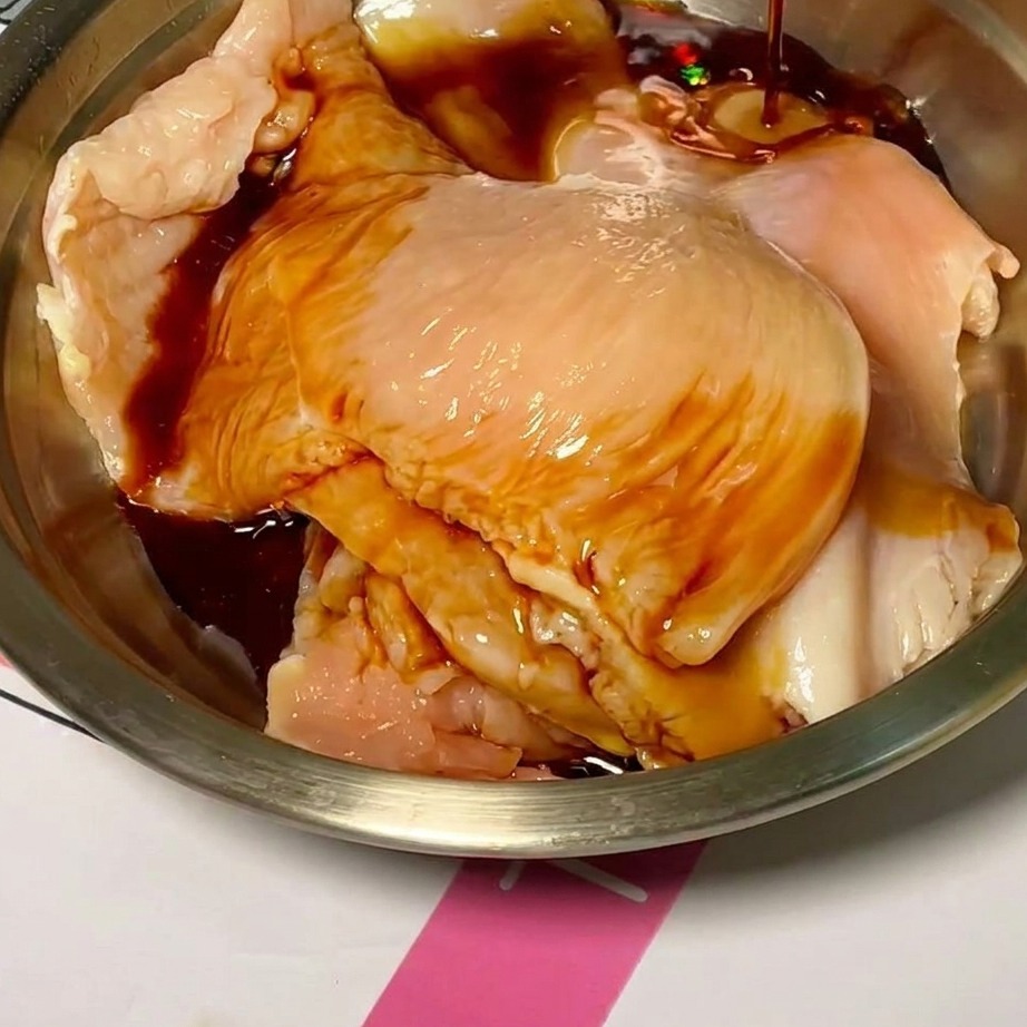 Lonchas de pollo crudo en un bol mezclándose con un adobo oscuro y sabroso.