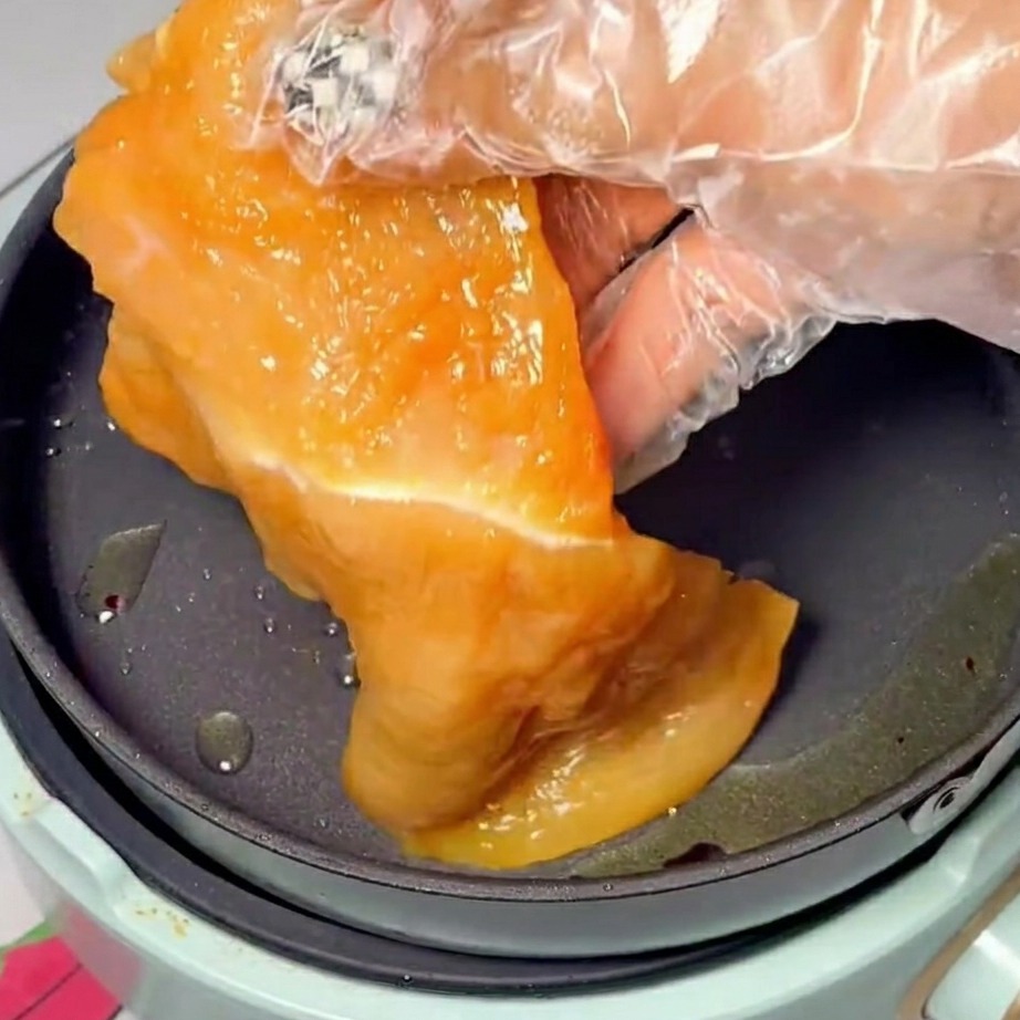 Lonchas de pollo marinado dorándose en una sartén caliente con aceite.