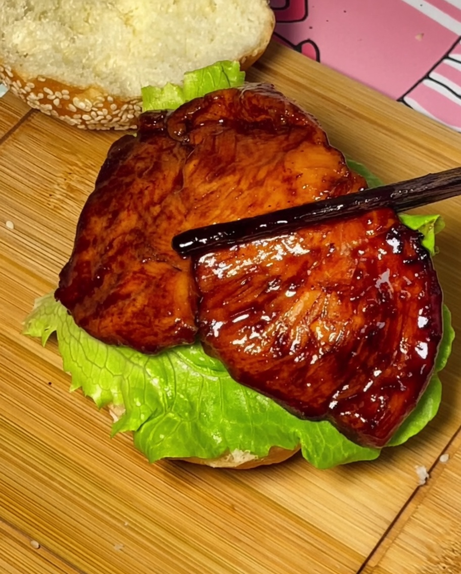 Pollo teriyaki, tomate y queso siendo colocados sobre el pan de hamburguesa.