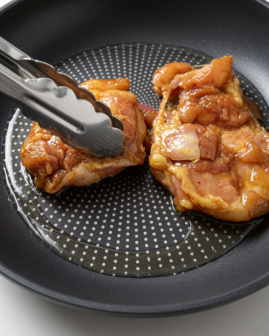 Muslos de pollo marinado colocándose en una sartén caliente con aceite usando pinzas de metal.