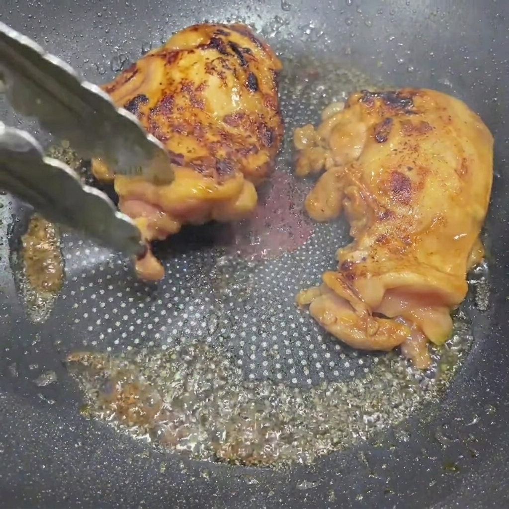 Muslos de pollo glaseados siendo volteados en la sartén con pinzas.