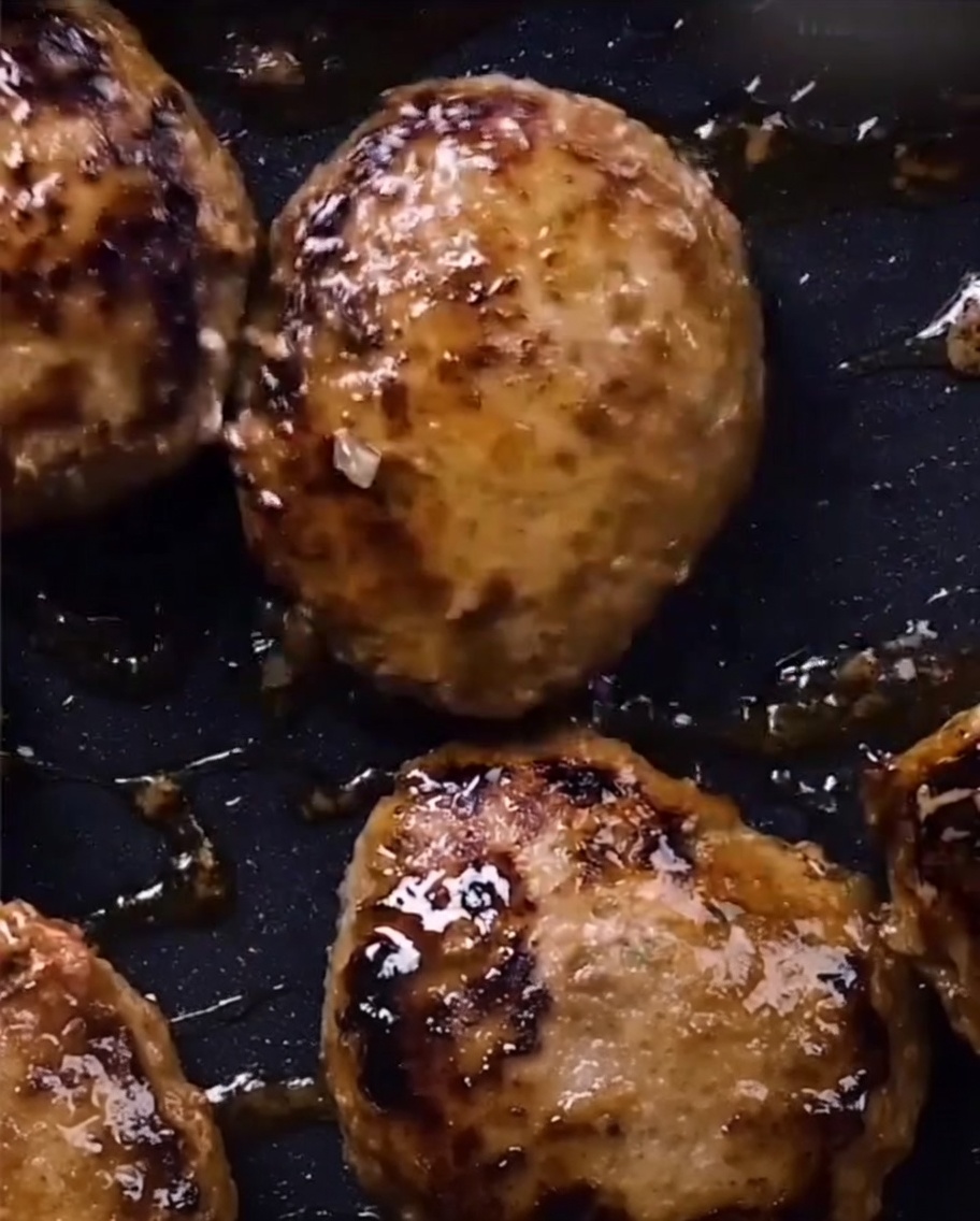 Hamburguesas brillantes con un espeso glaseado teriyaki en una sartén.