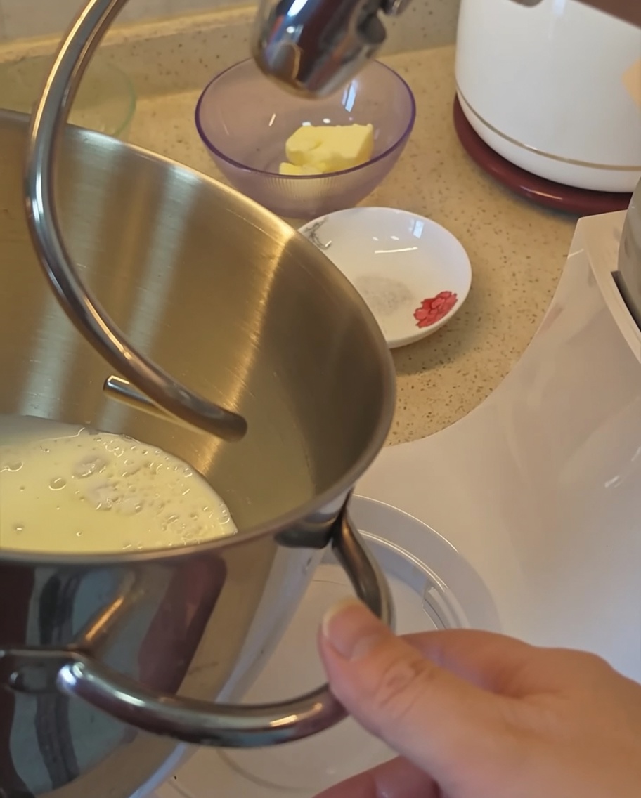 Vista cercana del bol de la amasadora con los ingredientes secos y la leche para la masa del pan.