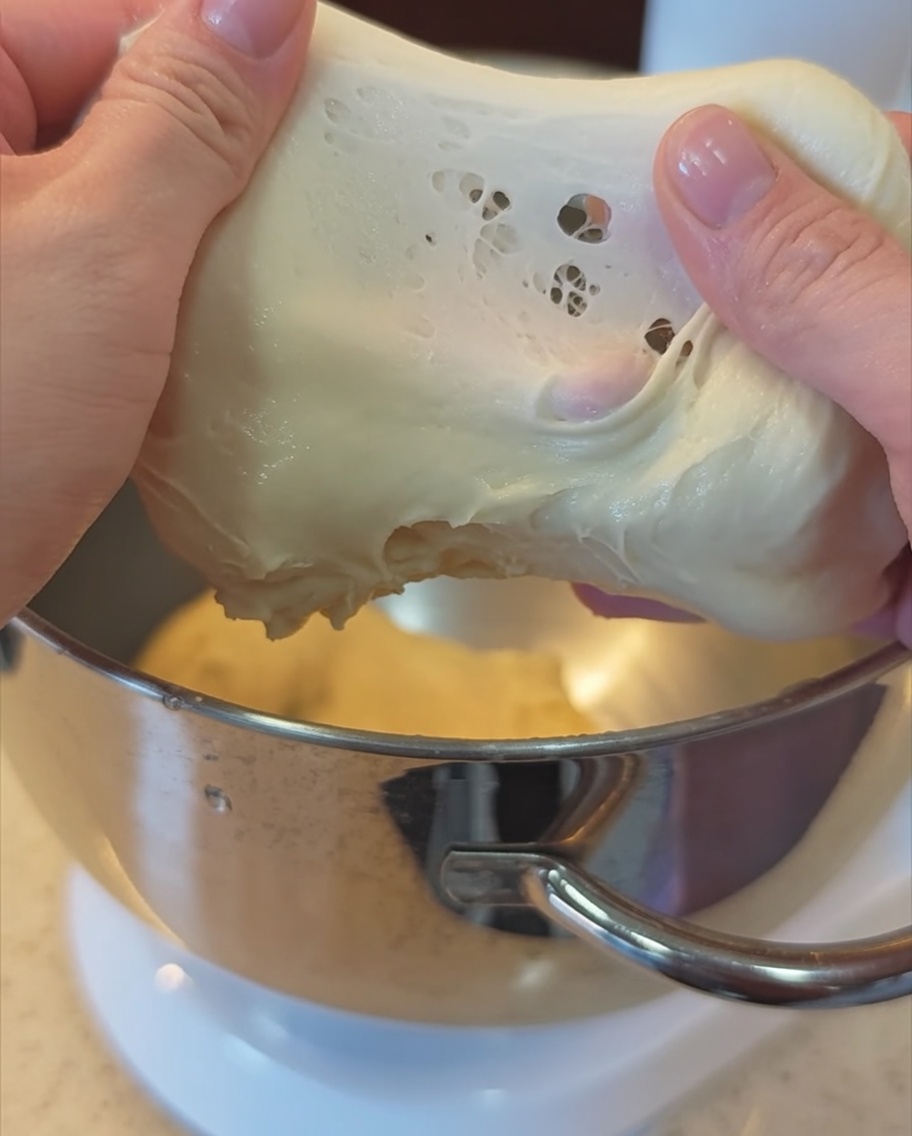 Un par de manos estirando un trozo de masa lisa y elástica para comprobar el punto de membrana.
