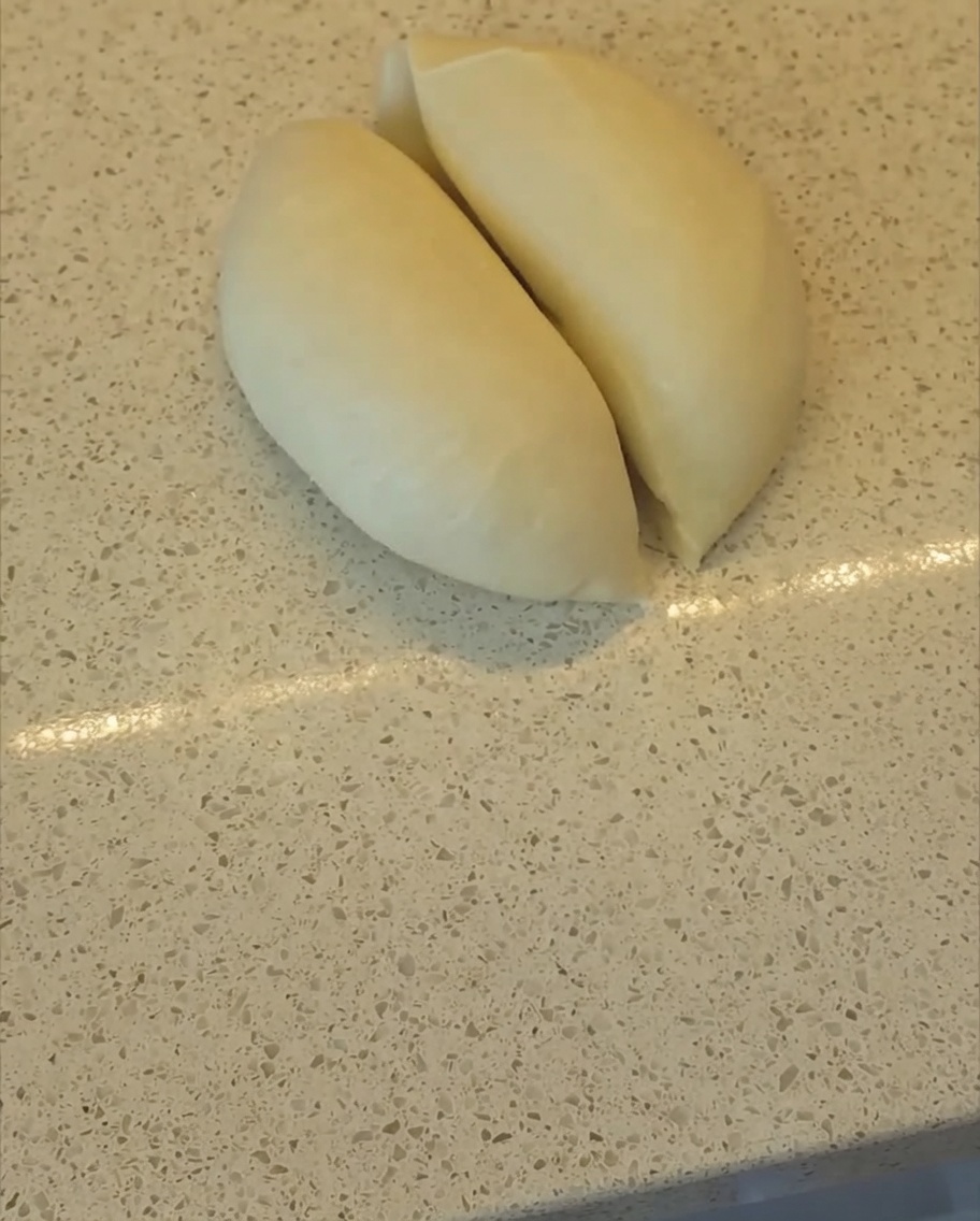Una rasqueta de panadero cortando una masa lisa en dos mitades iguales sobre la encimera de la cocina.