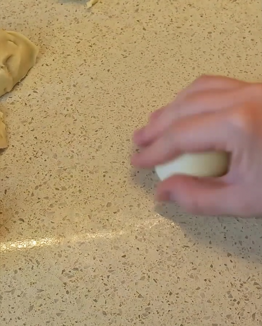 Una mano rodando una porción de masa sobre la encimera para darle forma de bola lisa y redonda.