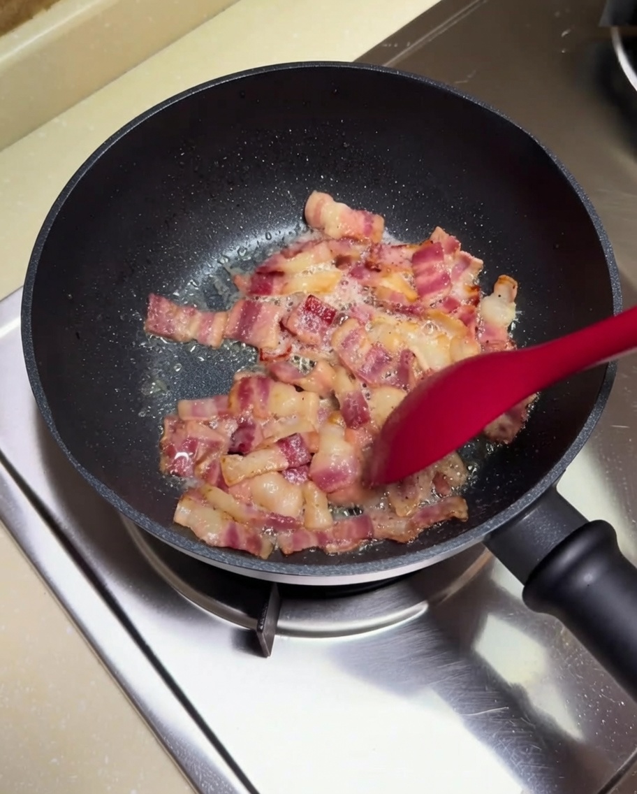 Añadiendo los dados de patata hervida a la sartén con el bacon frito.
