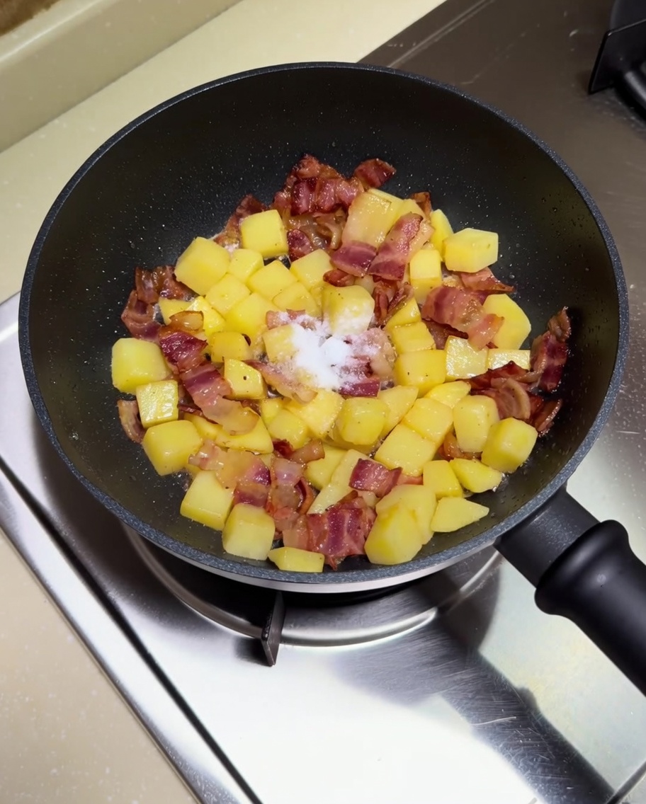 Añadiendo sal y salsa de soja a la sartén con patatas y bacon.