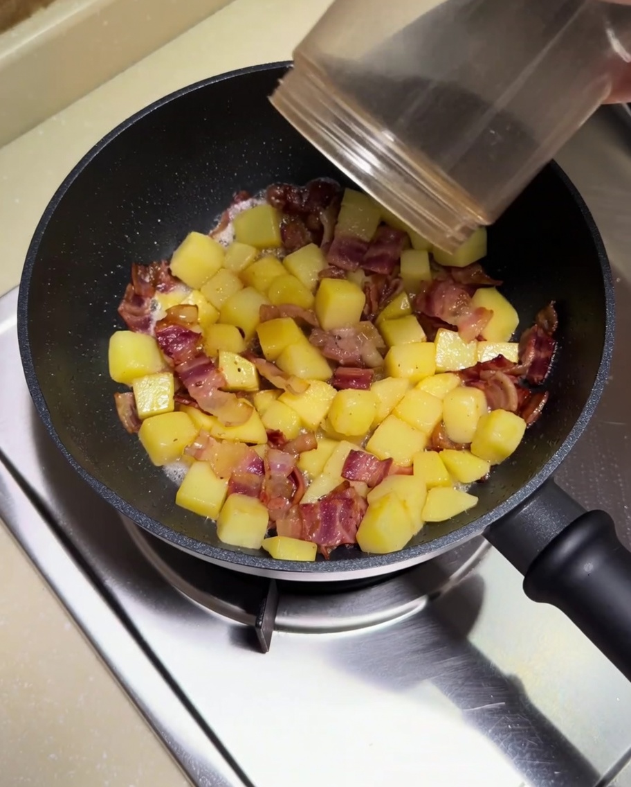 Espolvoreando chile y comino en polvo sobre el salteado de patatas y bacon.