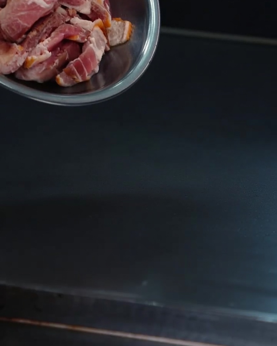 Trozos de bacon crujiente friéndose en una plancha caliente.