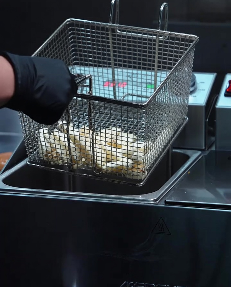 Patatas fritas doradas y crujientes siendo levantadas de una freidora en una cesta de metal.