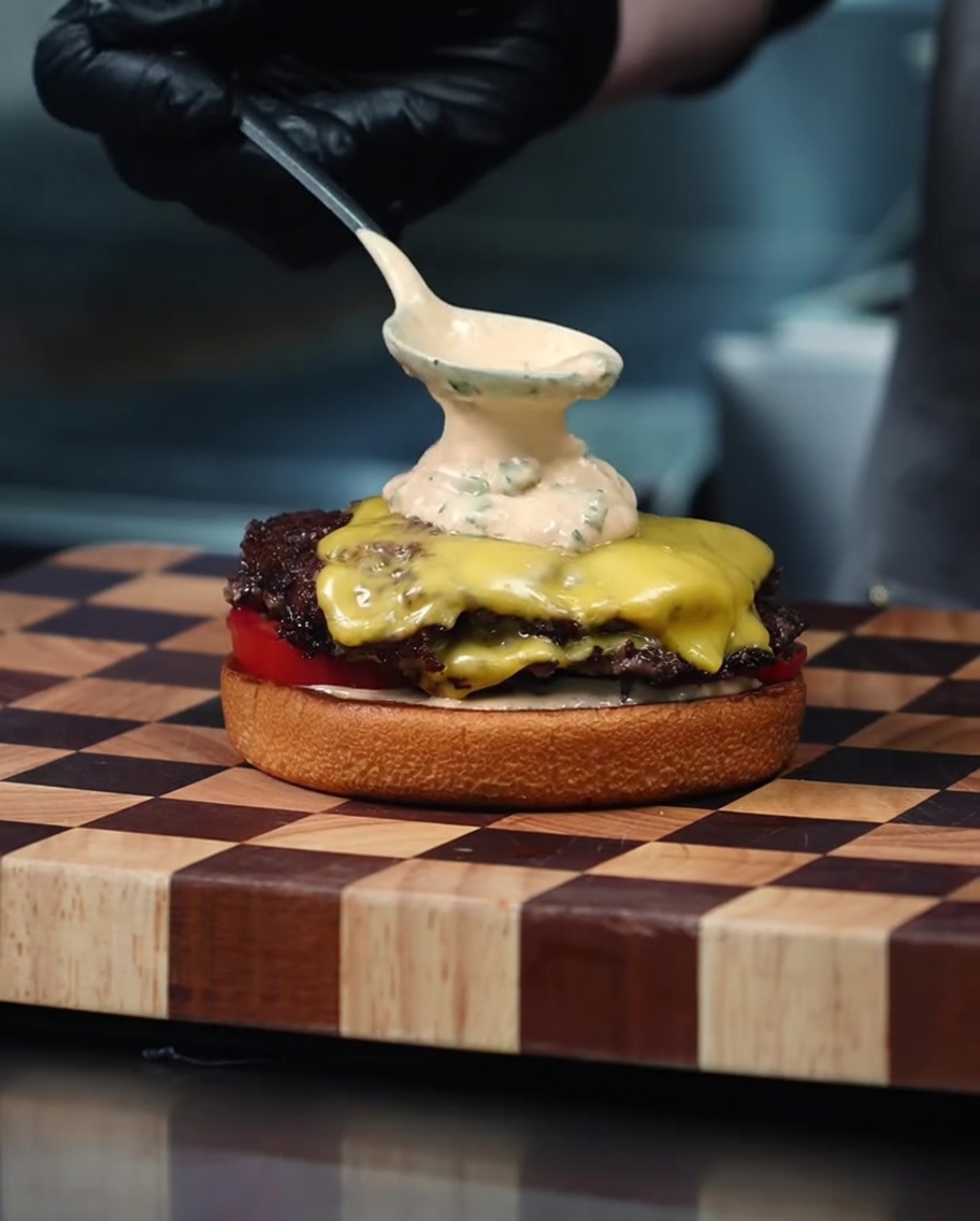 Primer plano de trozos de bacon crujiente espolvoreados sobre queso cheddar fundido en una hamburguesa.