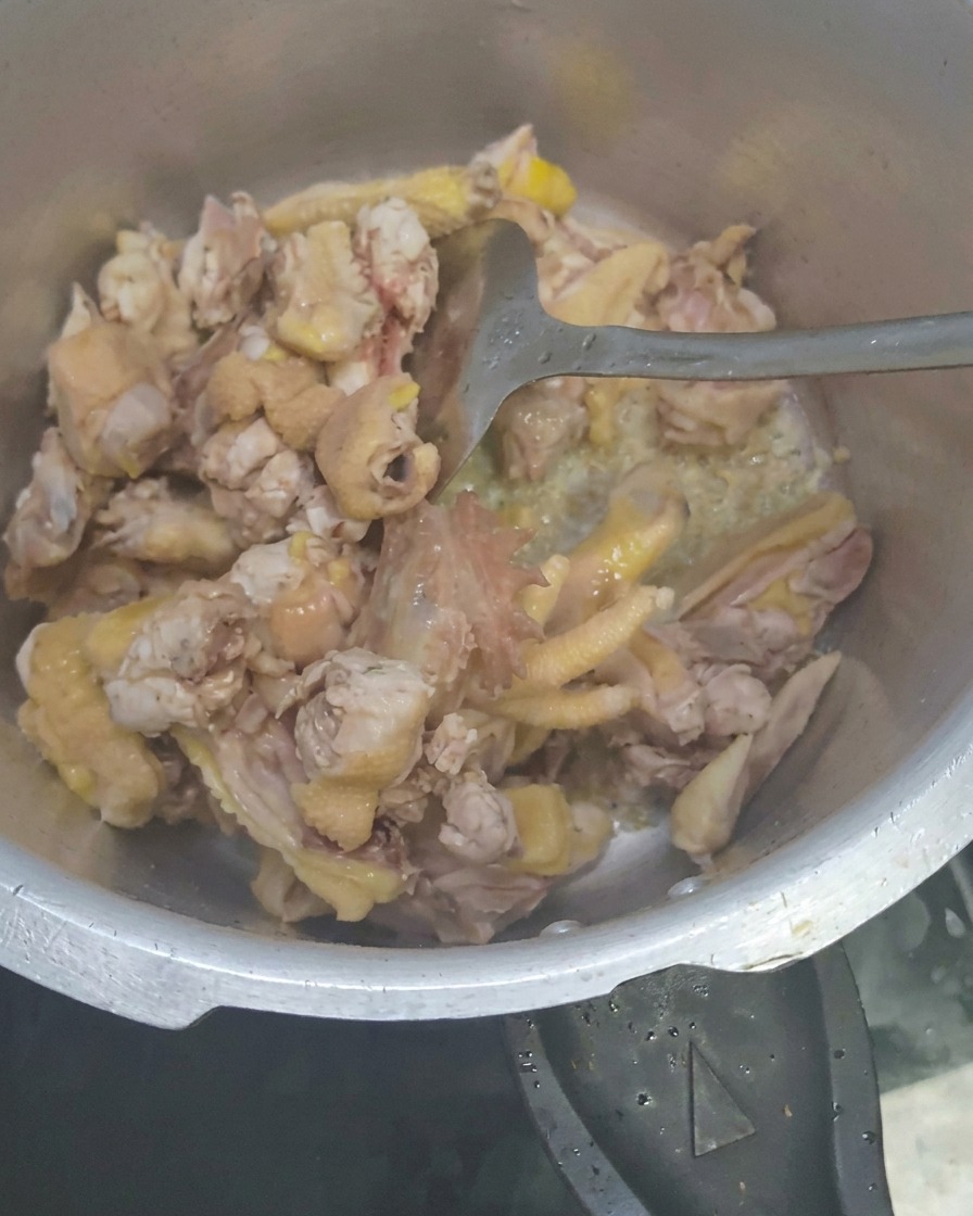 Rodajas de galanga siendo mezcladas con la preparación de pollo.