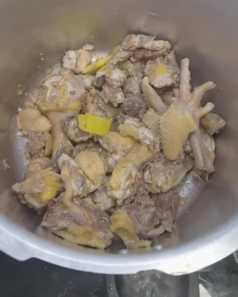 Agua siendo vertida en la olla a presión sobre el pollo y los ingredientes aromáticos.