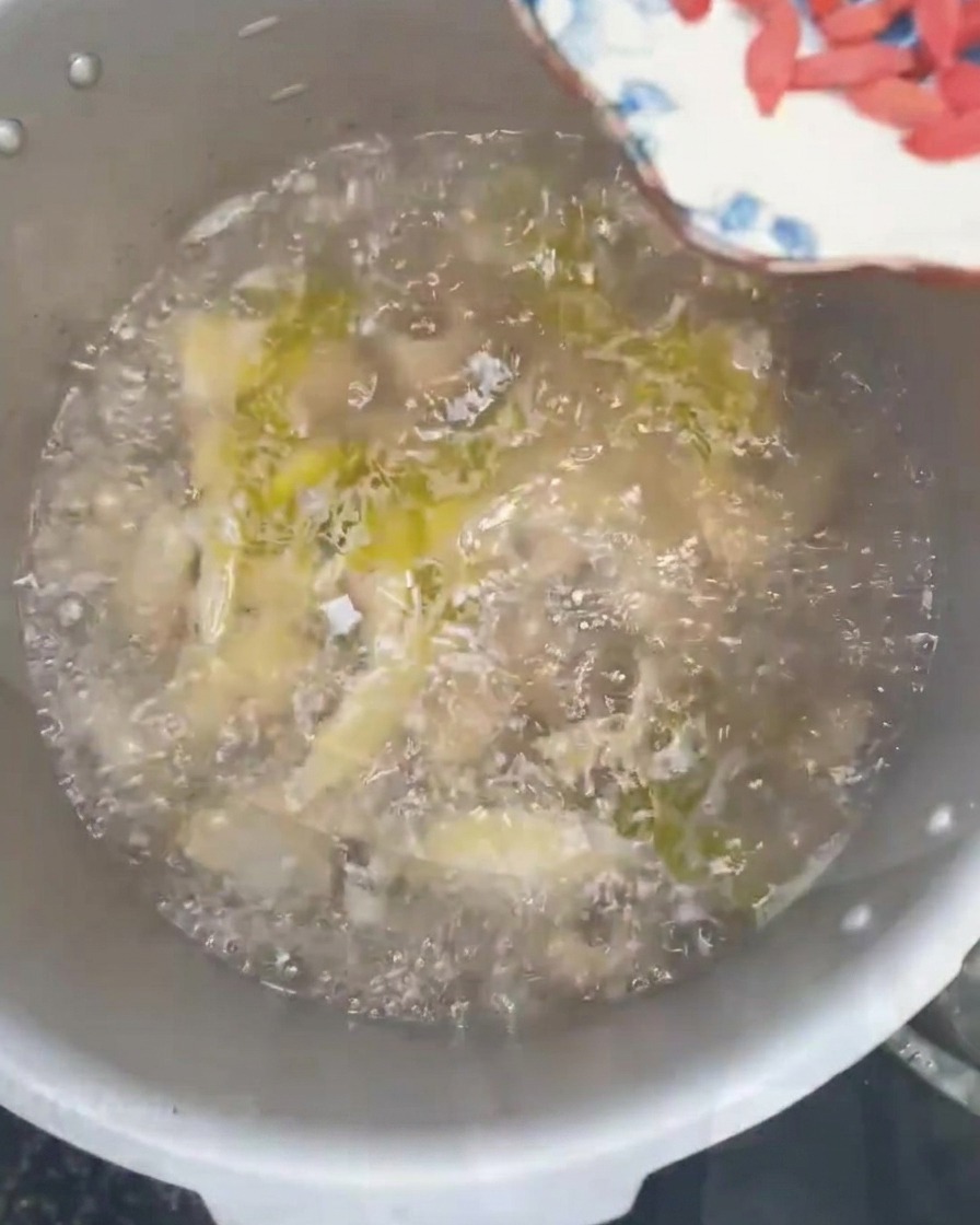 Bayas de goji y cebollín fresco picado siendo espolvoreados en una olla de sopa de pollo burbujeante.