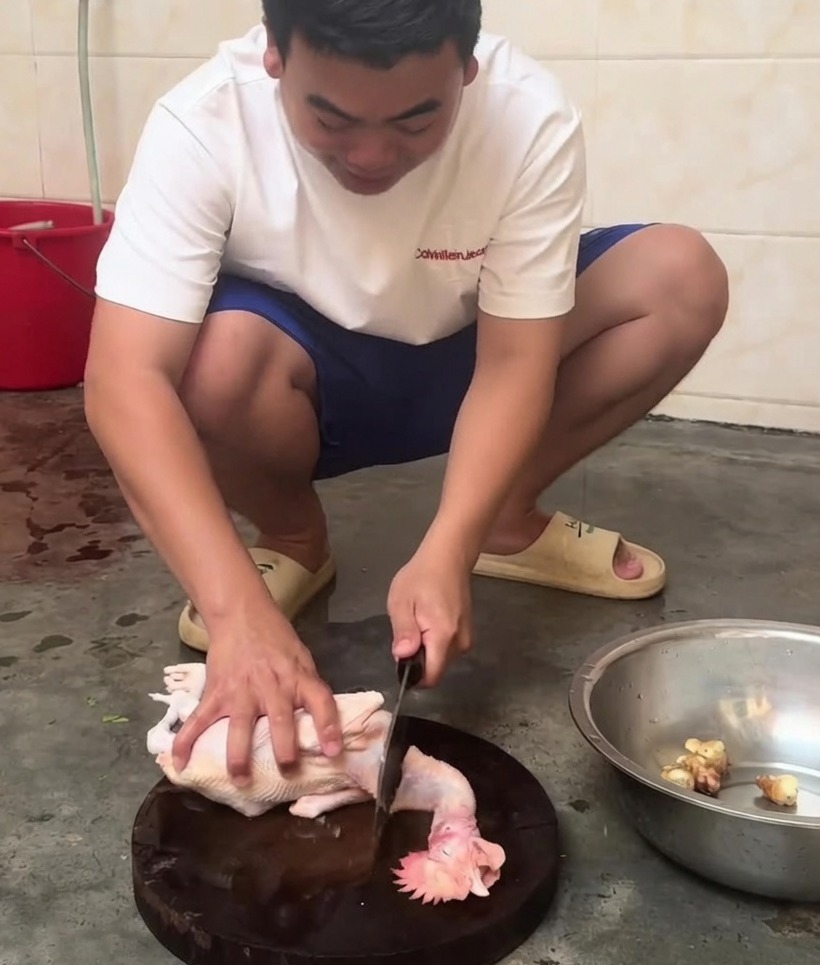 Un pollo entero crudo siendo cortado en trozos más pequeños con un cuchillo de carnicero sobre una tabla de madera.