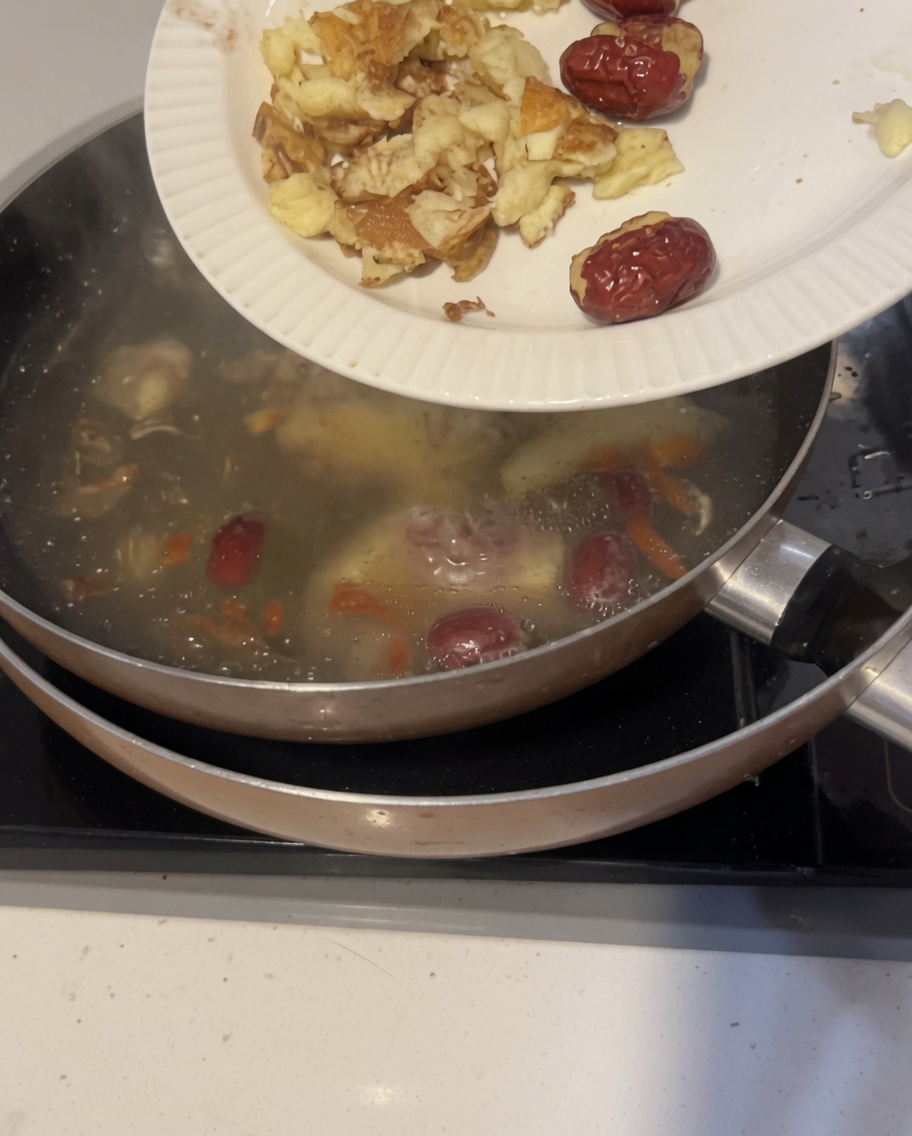 Un primer plano de jengibre de arena machacado y dátiles rojos flotando en una olla con agua fría.
