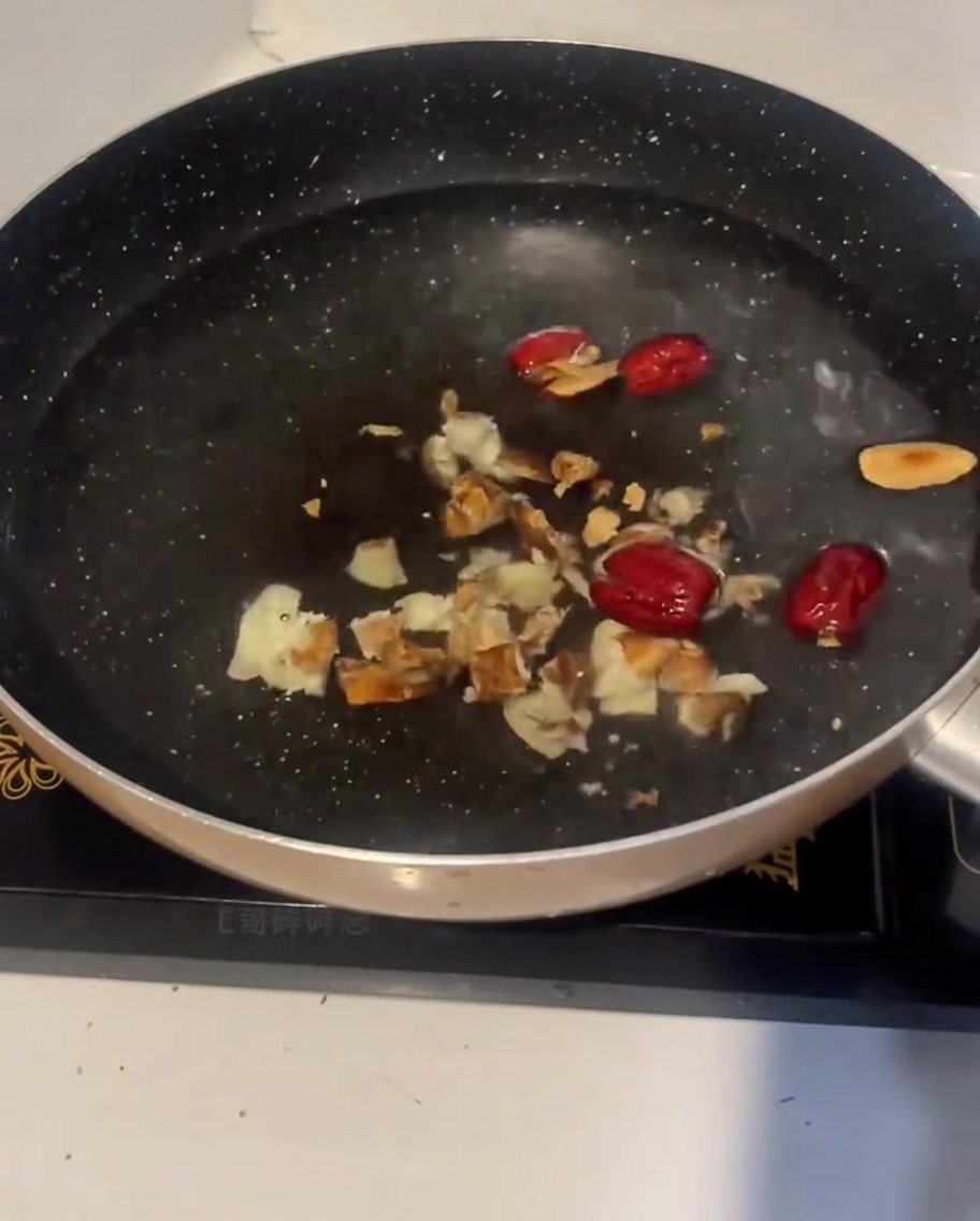 Trozos de pollo crudo siendo añadidos a la olla de agua fría con jengibre y dátiles rojos.