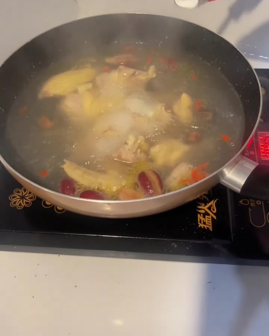 Una cucharada de sal siendo añadida a la sopa de pollo hirviendo para sazonarla.