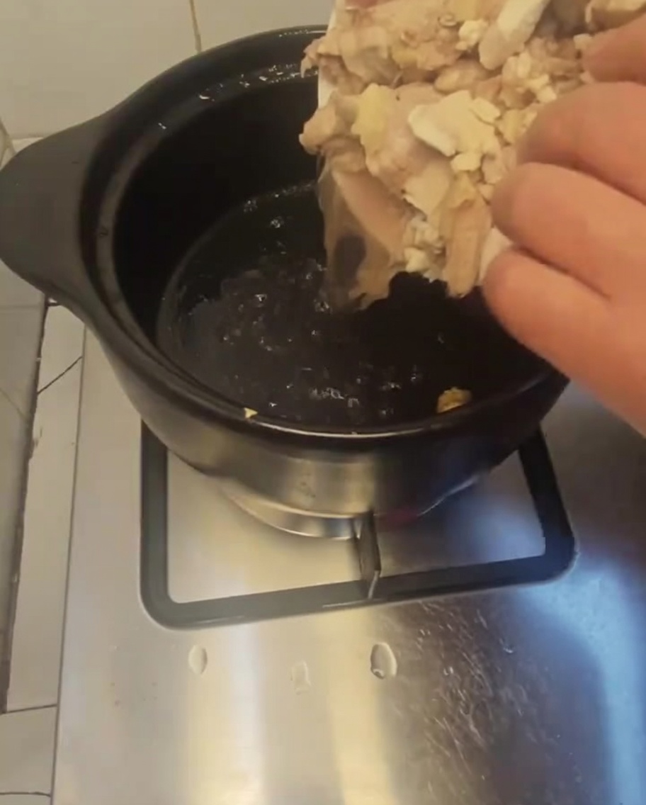 Piezas de pollo escaldadas vertiéndose desde un plato blanco a una olla de barro oscura precalentada.