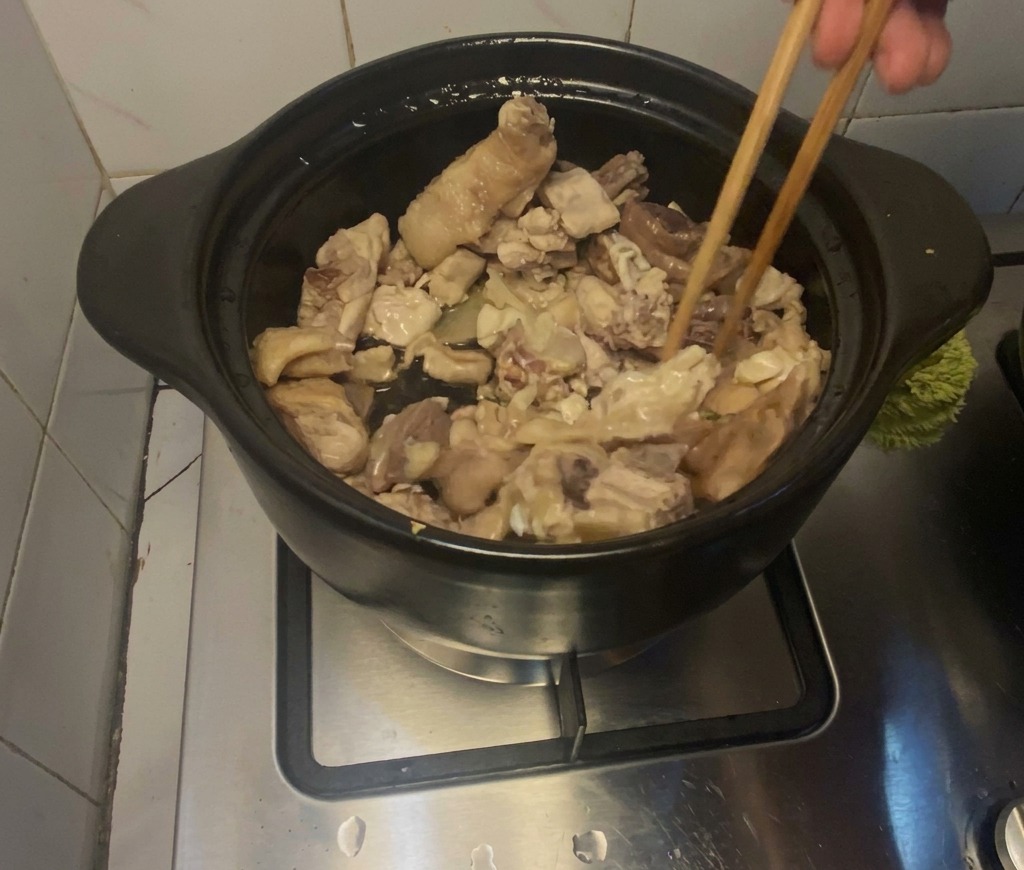 Piezas de pollo sofriéndose activamente con palillos de madera dentro de una olla de barro negra.