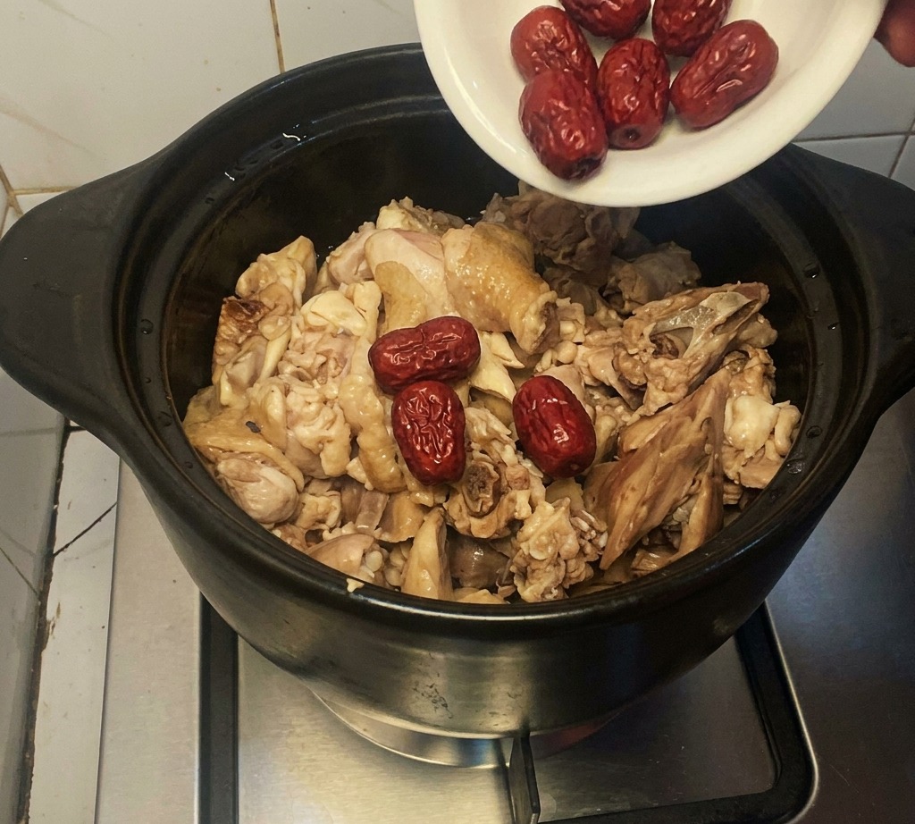 Un pequeño plato blanco vertiendo dátiles rojos secos en una olla de barro con pollo.