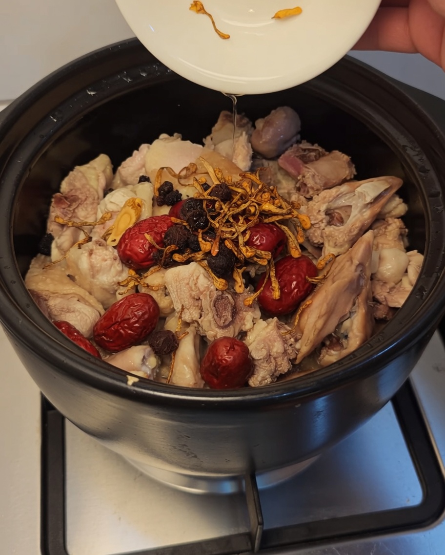 Flores de cordyceps, bayas de goji oscuras y longan siendo añadidos a la olla.