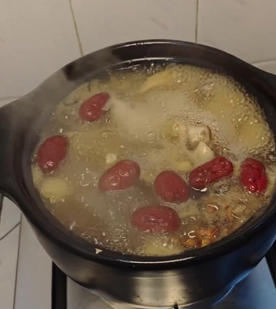 Sopa de pollo hirviendo vigorosamente en una olla de barro con dátiles rojos flotando.