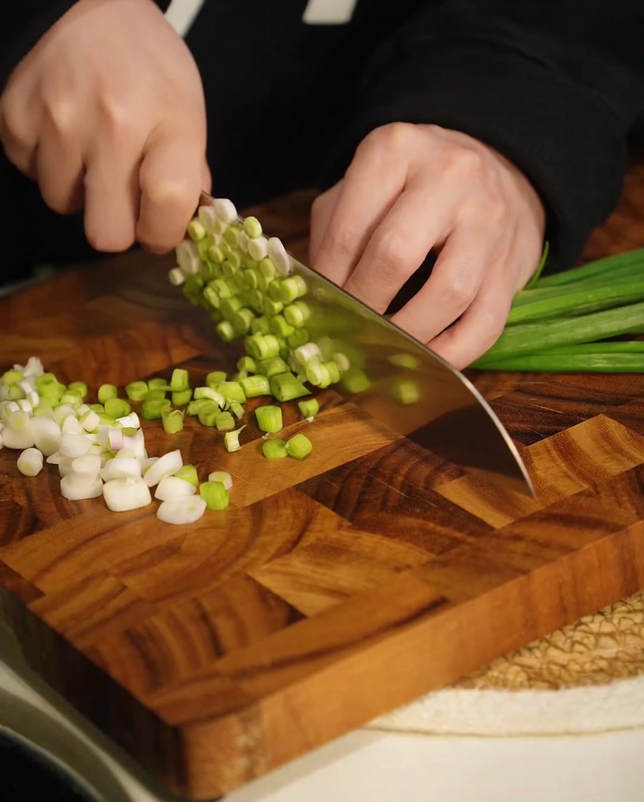 Cebolletas verdes recién picadas sobre una tabla de cortar de madera.