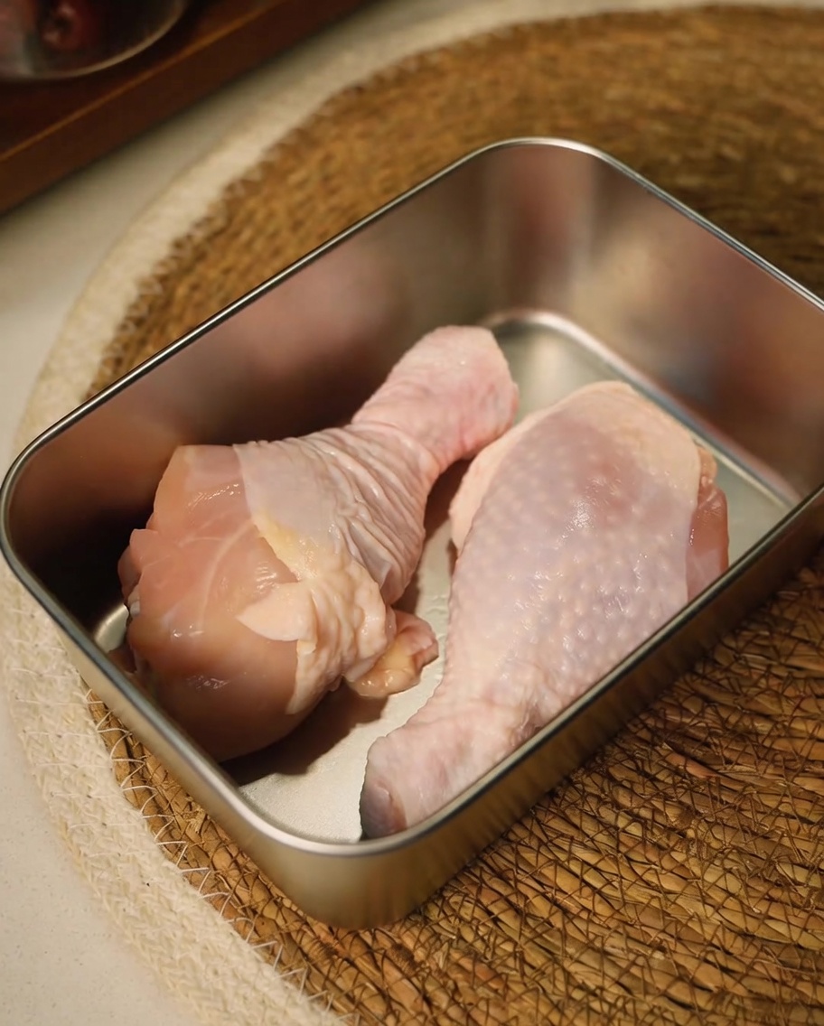 Muslos de pollo crudos siendo recortados con tijeras de cocina en un recipiente de metal.