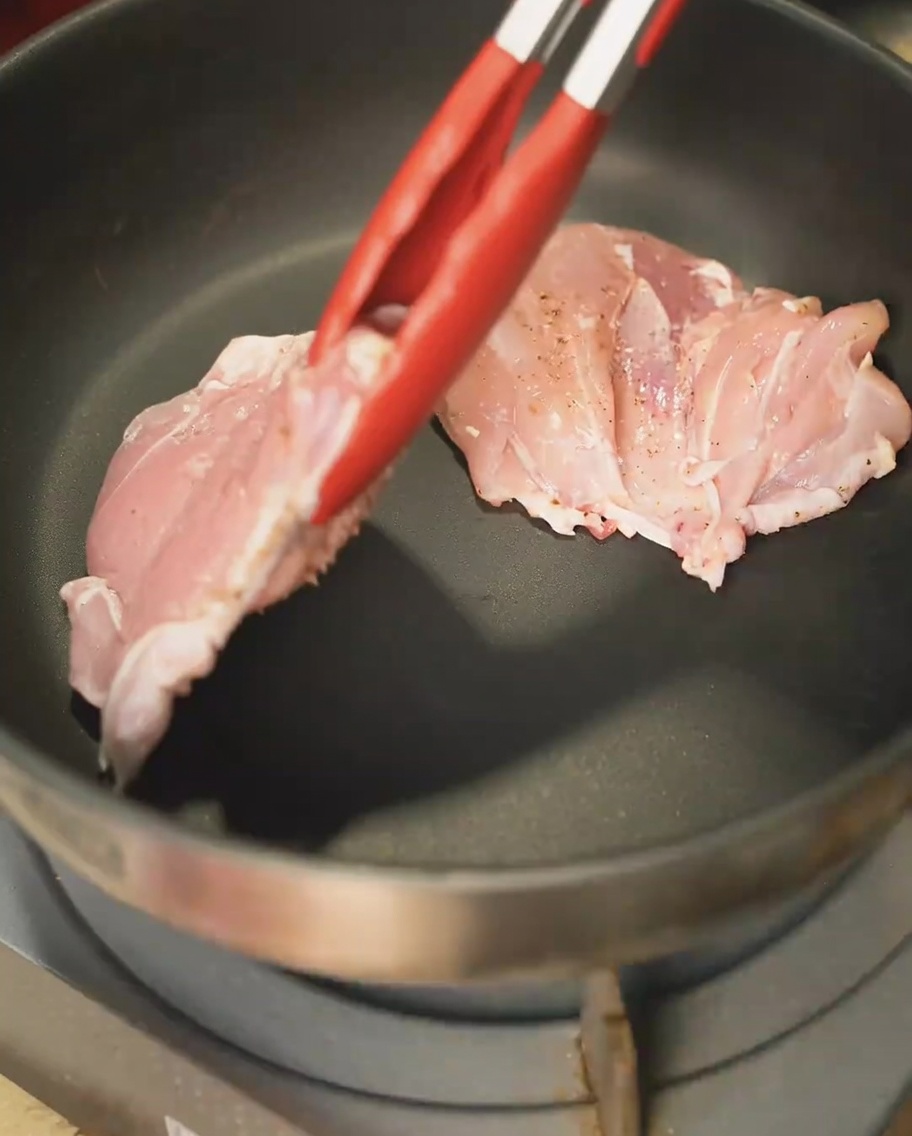 Muslos de pollo dorándose en una sartén, con la piel hacia abajo, logrando una costra dorada.