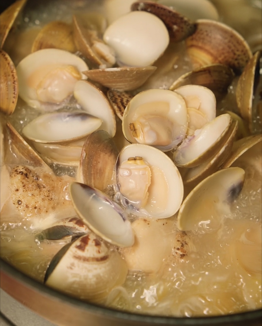 Almejas frescas siendo añadidas a la olla de sopa de pollo y cebolla para cocinar al vapor.
