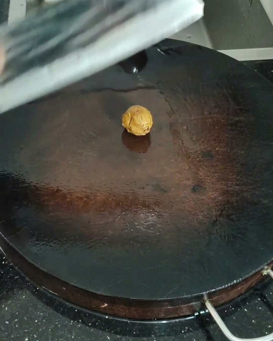 Primer plano de jengibre de la arena siendo aplastado con el lateral de un hacha de cocina sobre una tabla de madera.