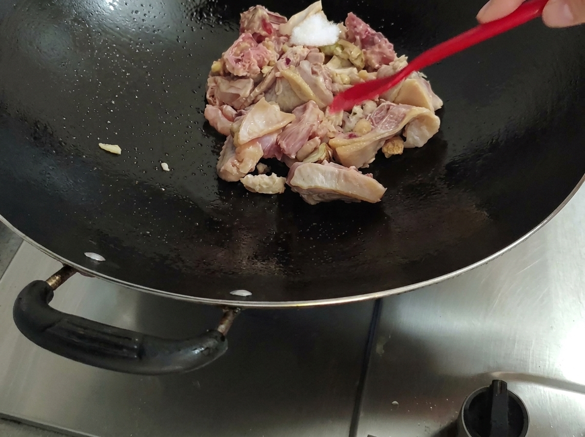 Añadiendo sal al pollo dentro del wok con una espátula roja.