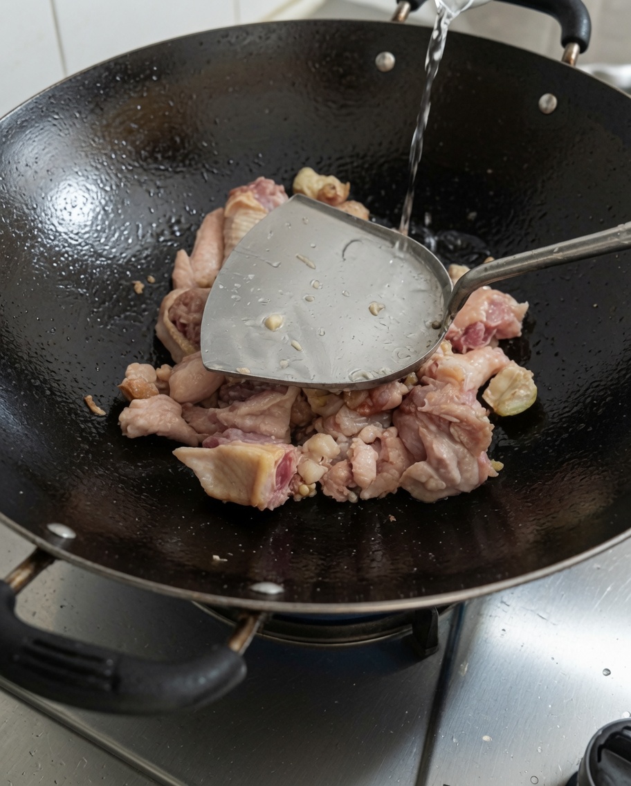 Vertiendo agua fresca en el wok que contiene el pollo sellado.