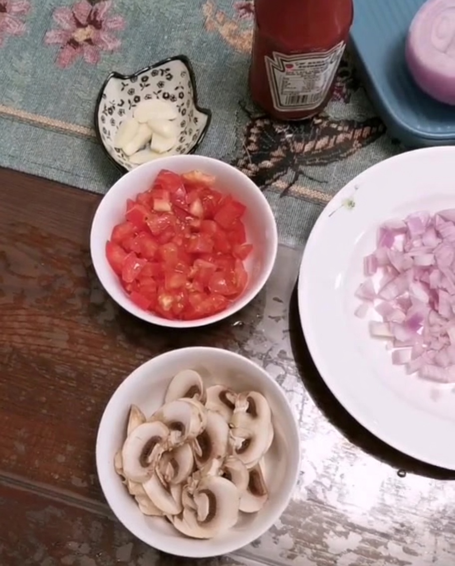 Un tazón con tomates picados, champiñones laminados y ajo picado sobre una mesa.