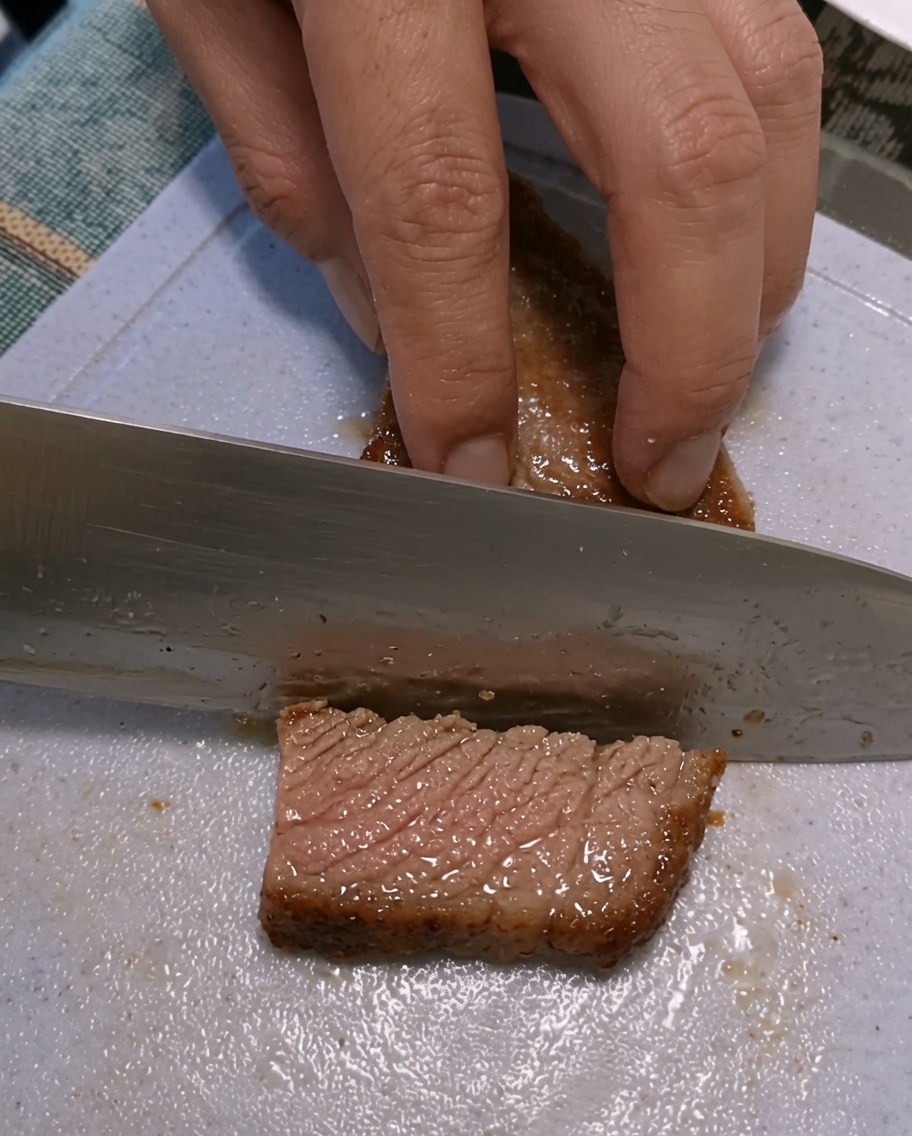 Manos cortando un filete sellado sobre una tabla de cortar de plástico.