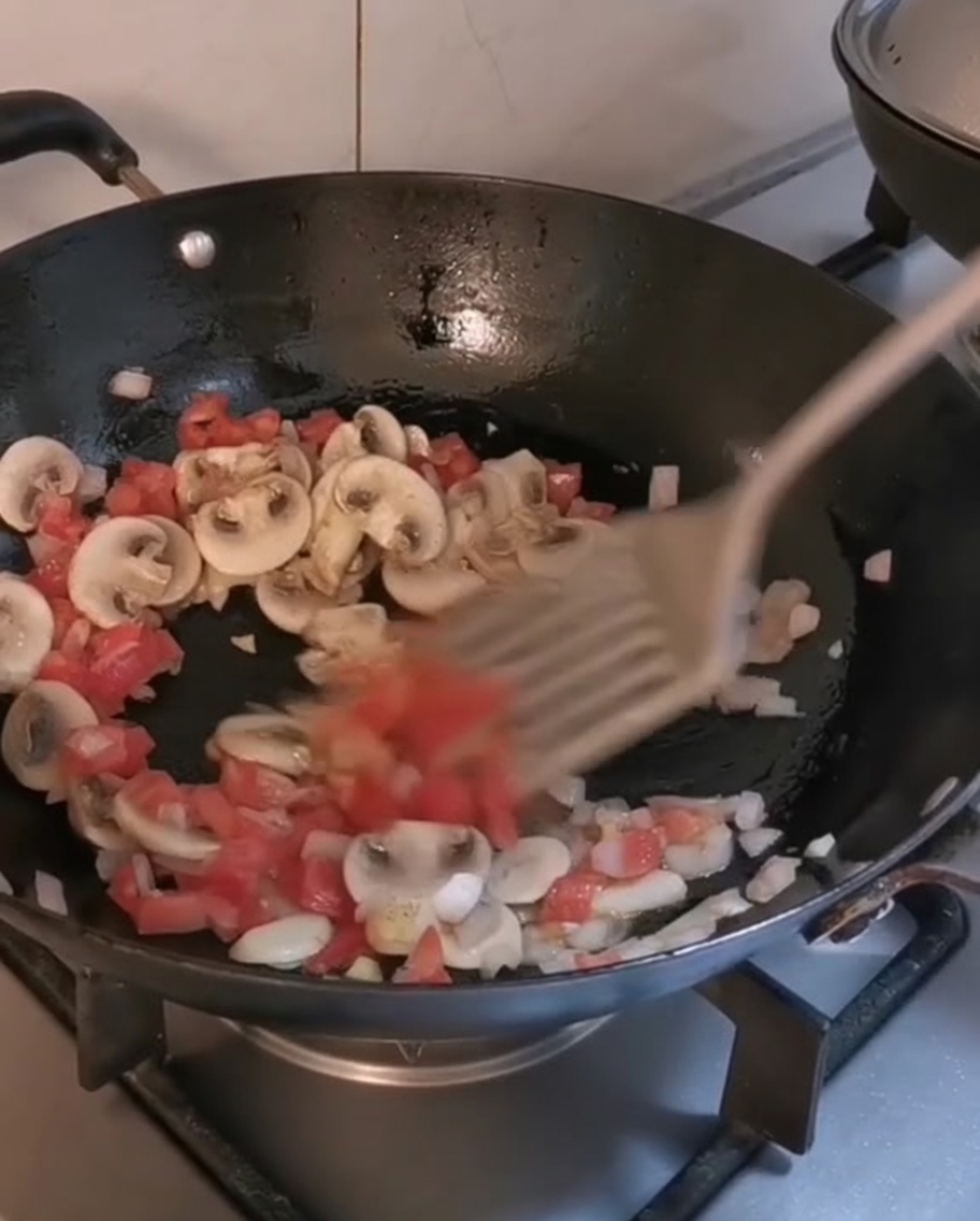 Mezclando pasta penne cocida y tiras de filete en un wok con vegetales salteados.