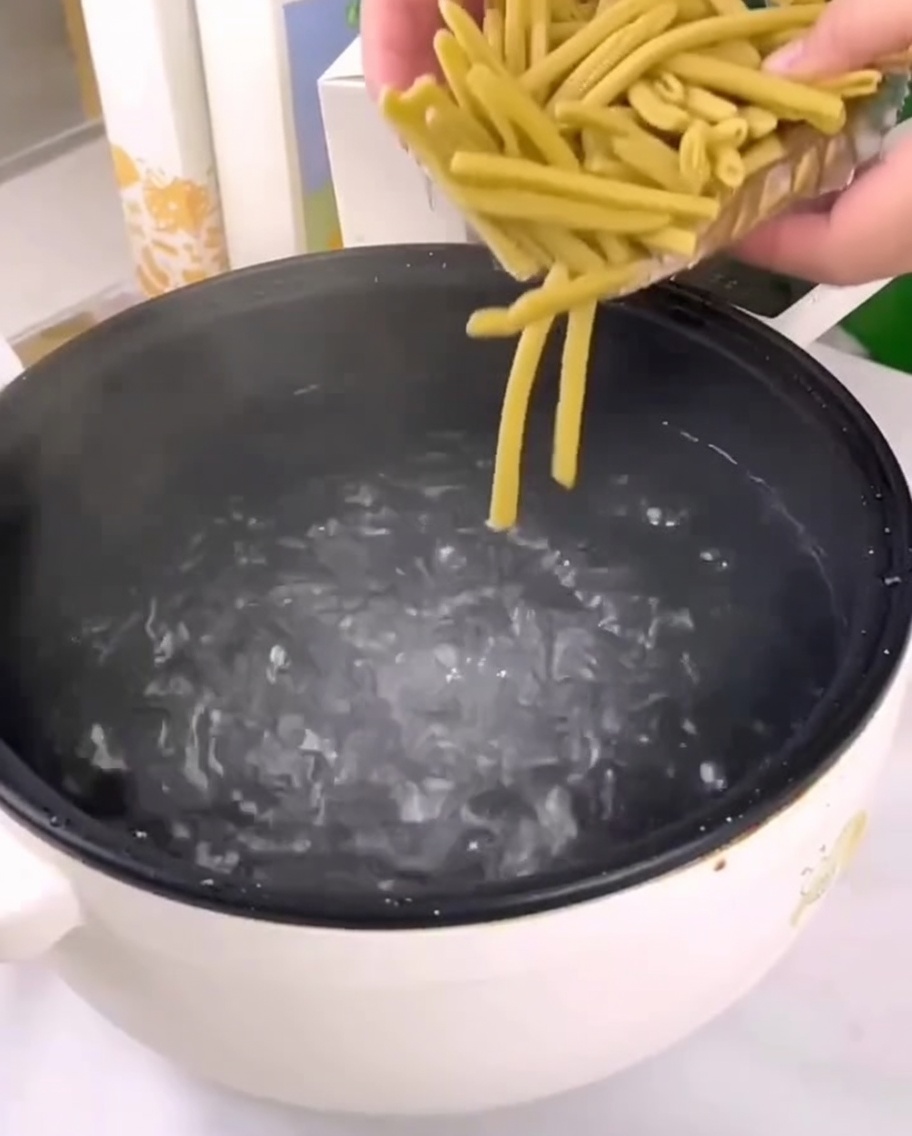 Pasta penne de mijo seca siendo vertida en una olla con agua hirviendo.