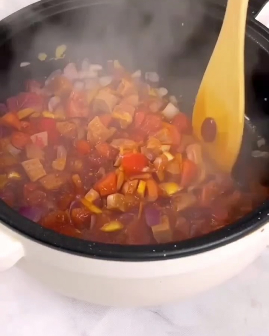 Tomates troceados, jamón y vegetales siendo salteados en una sartén con una espátula de madera.
