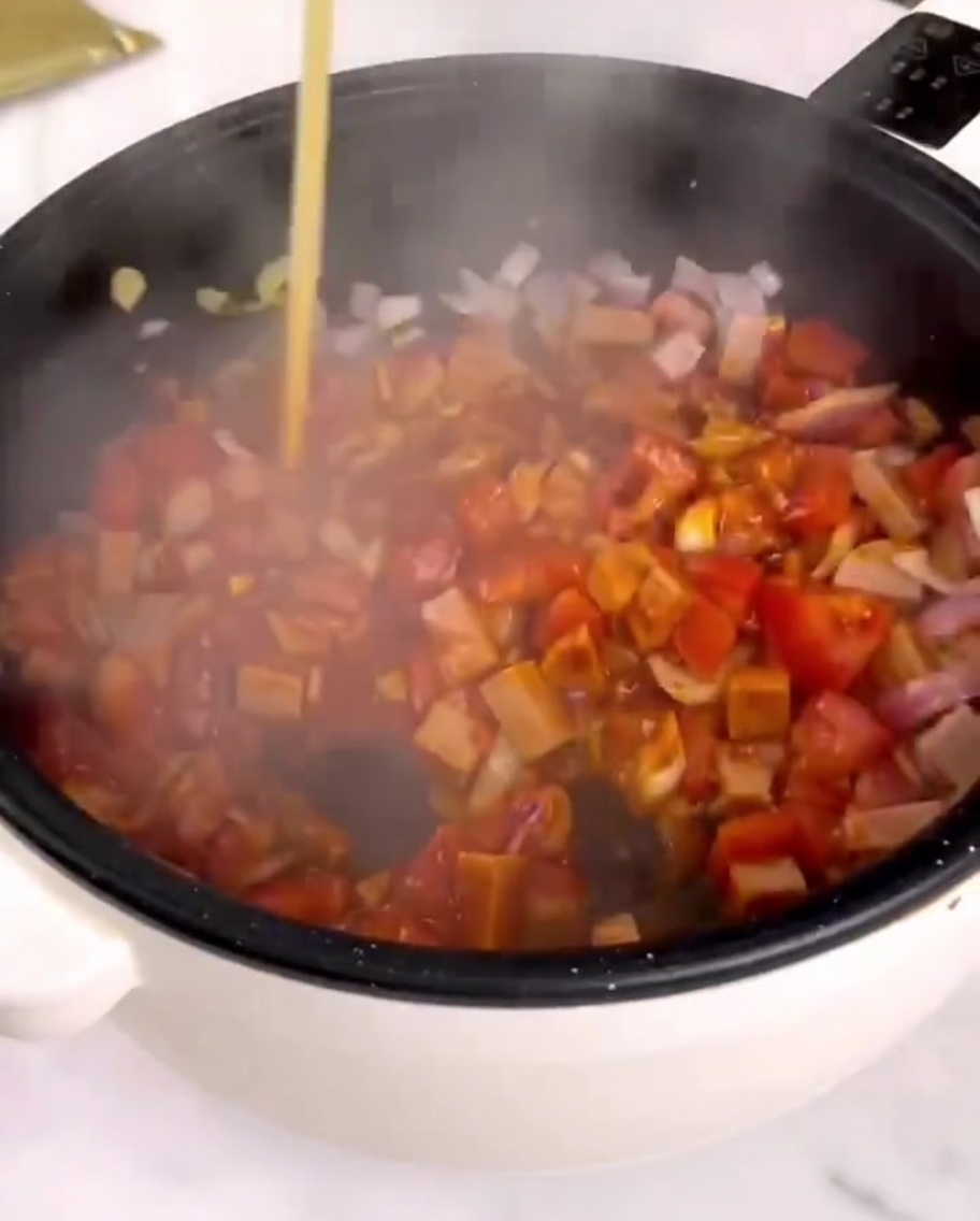 Salsa para pasta siendo vertida en una sartén con vegetales salteados y jamón.