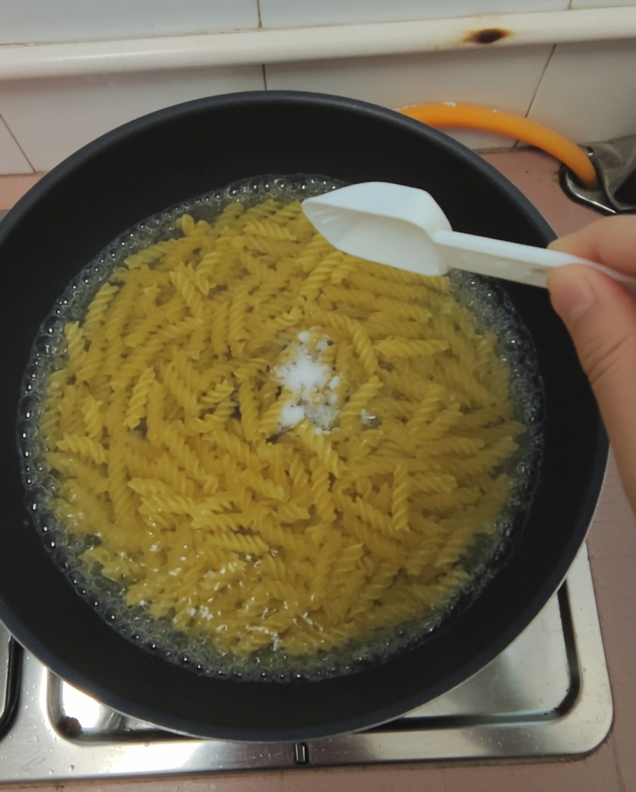 Una cucharada de sal siendo añadida a una olla con agua hirviendo.