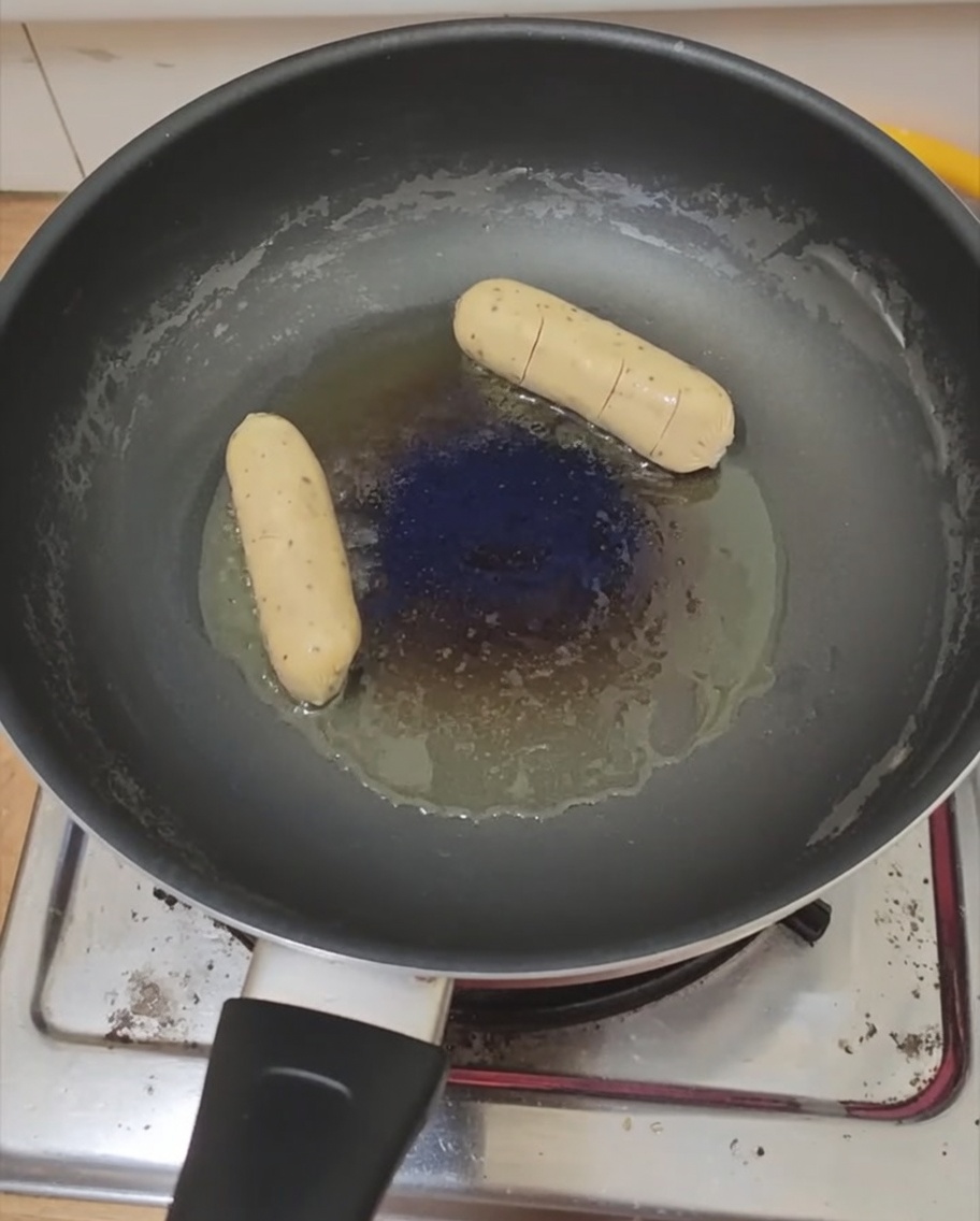Un huevo frito y una salchicha friéndose en una sartén.