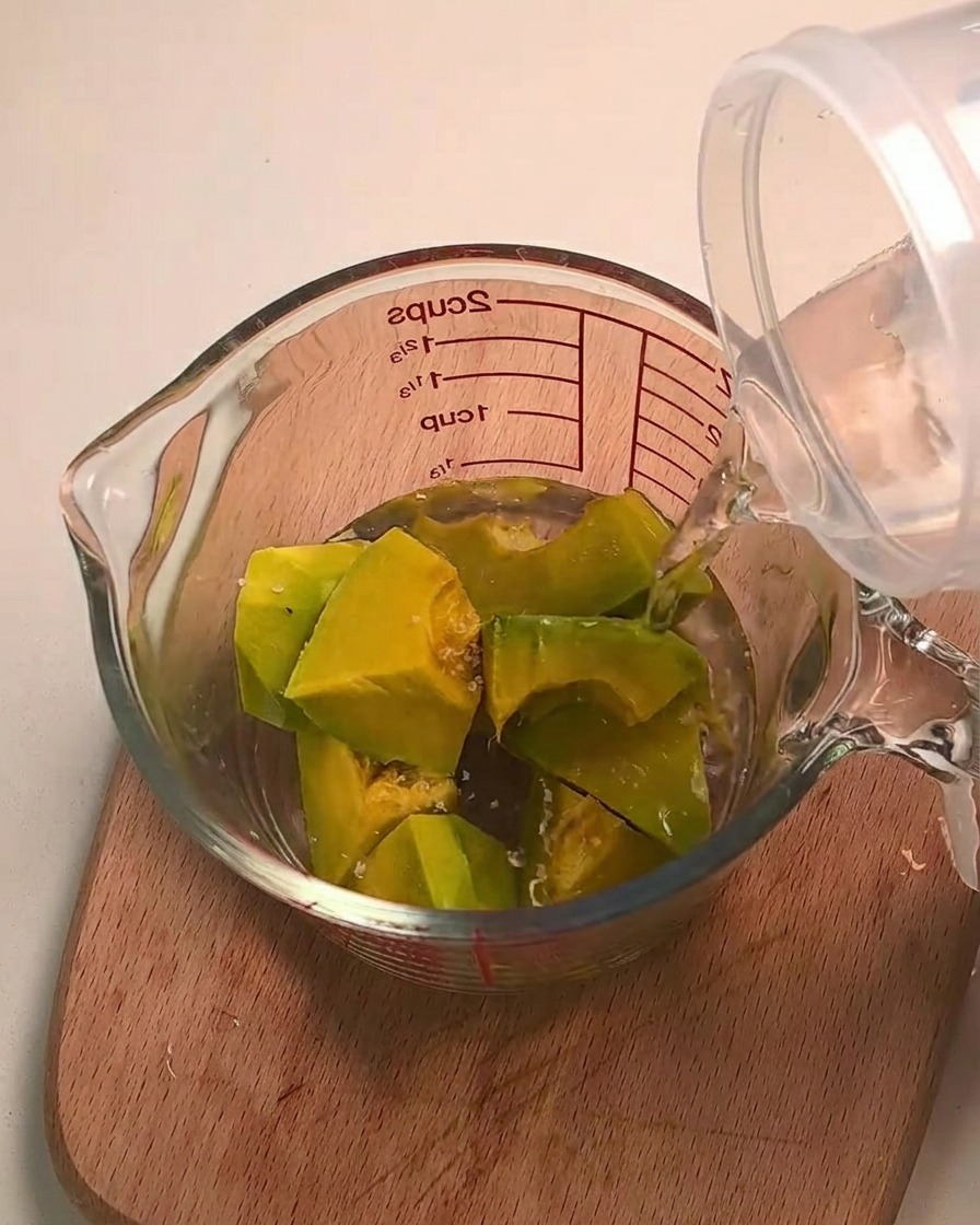 Agua vertiéndose sobre trozos de calabaza kabocha en una taza medidora de vidrio.