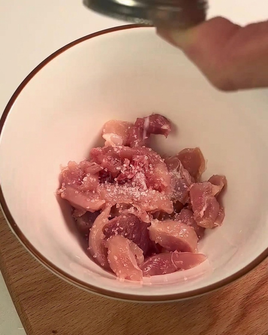 Carne de pierna de pollo siendo sazonada con sal y jugo de limón en un tazón blanco.