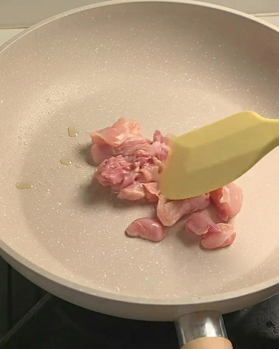 Trozos de carne de pierna de pollo sazonados salteándose en una sartén antiadherente, mostrando un ligero dorado.