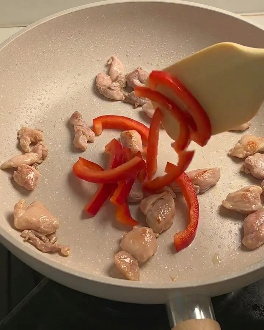 Pollo salteado, pimientos rojos en rodajas y champiñones cocinándose juntos en una sartén.